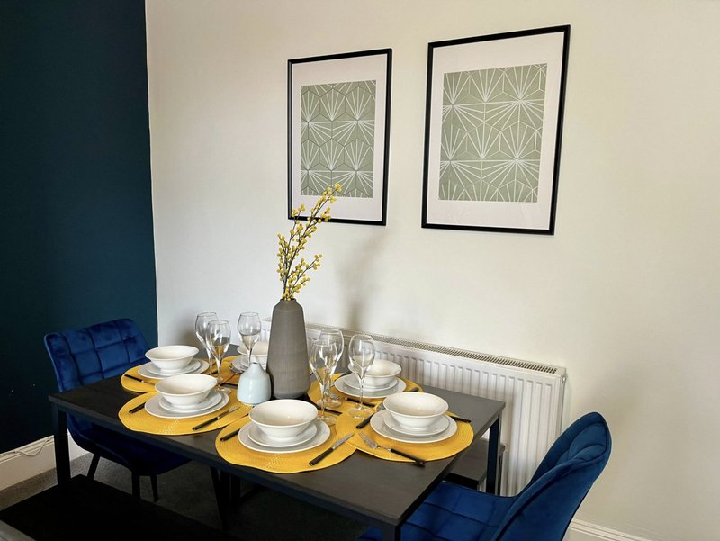 Dining table set with white dinnerware, yellow runner, and blue chairs