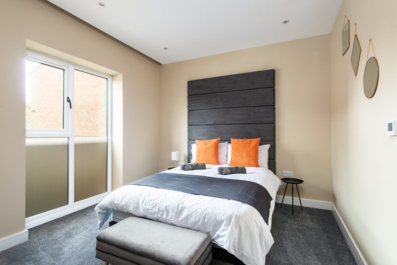 Modern bedroom with double bed, black headboard, orange pillows, and patio door