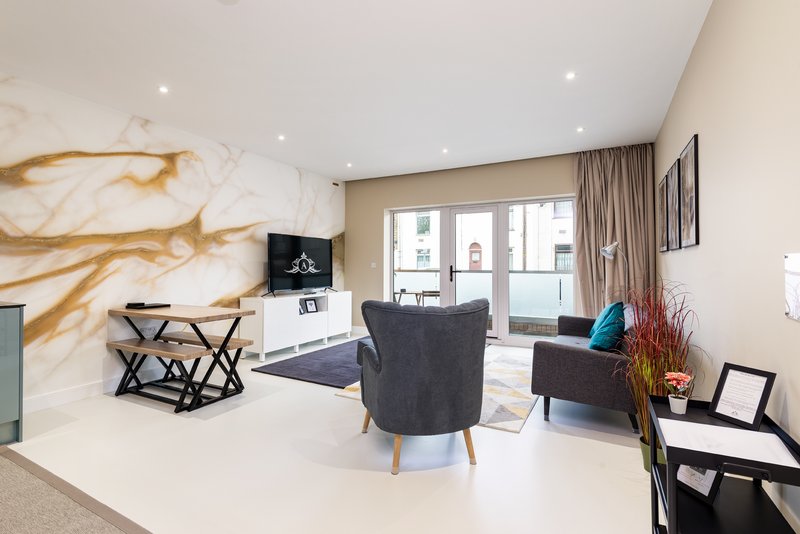 Modern living room with grey armchair, geometric coffee table, marble accent wall and floor-to-ceiling windows