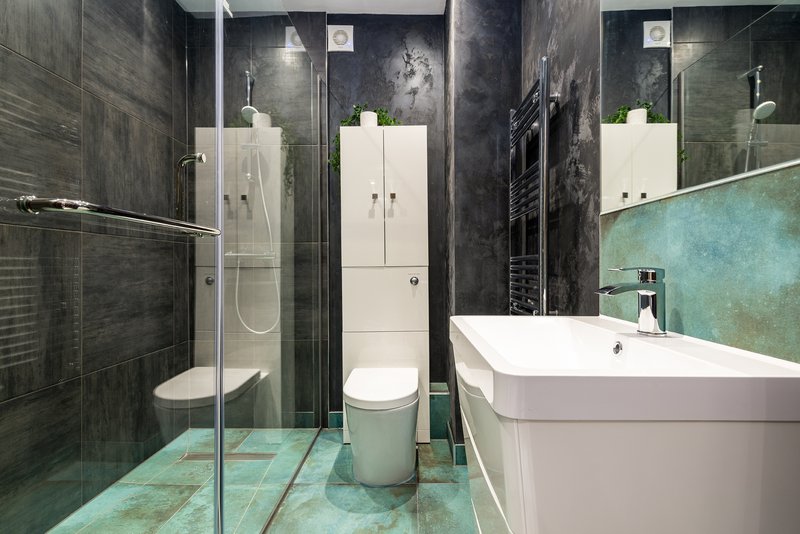 Modern bathroom with walk-in shower, freestanding bathtub, dual toilets, dark tile walls and turquoise floor