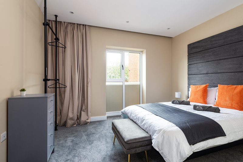 Modern bedroom with double bed, orange pillows, dark headboard and patio doors