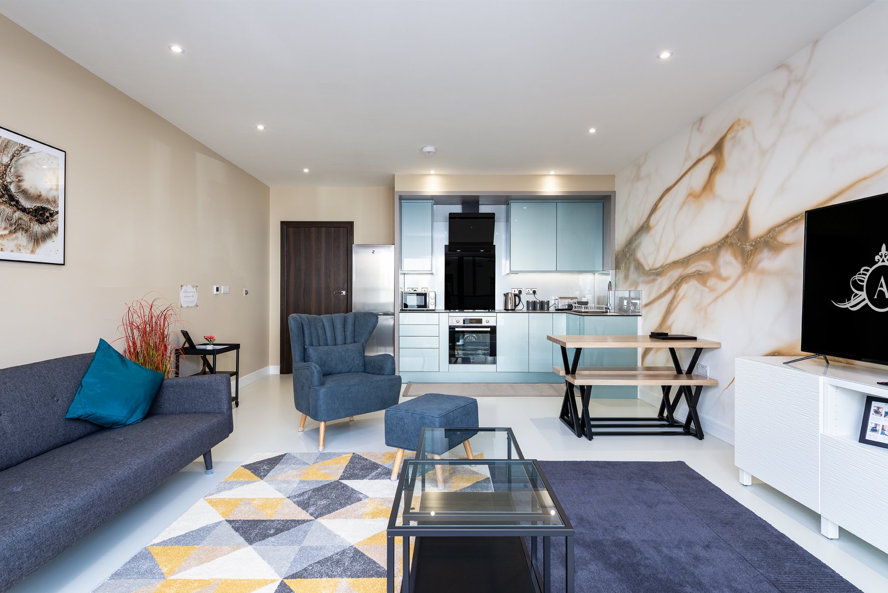 Open-plan living room with blue sofa, kitchen area, marble wall feature, and TV mounted on wall