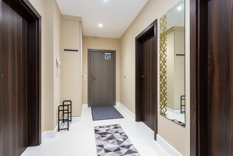 Hallway with dark wooden doors, cream walls, white flooring and geometric patterned runner rug