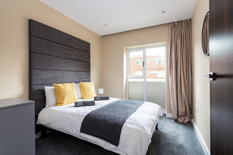 Modern bedroom with double bed, dark headboard, yellow cushions, and balcony door