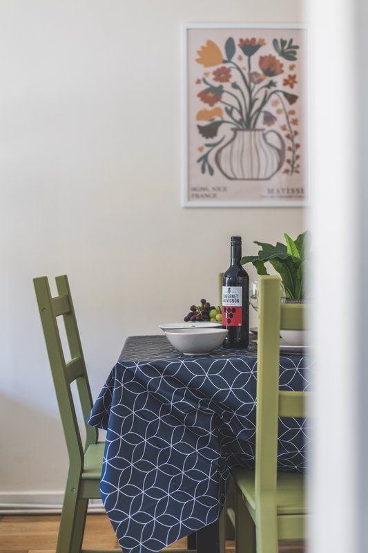 Dining table with green chairs, wine bottle, bowl, potted plant, and framed floral art on wall