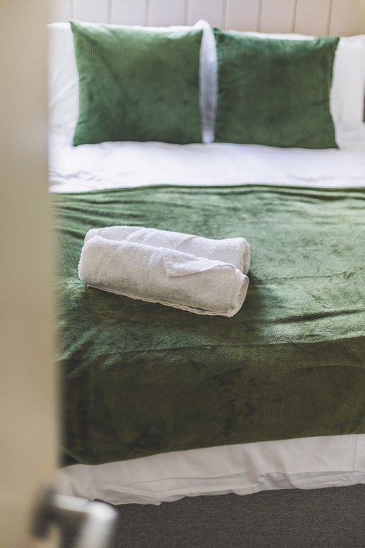 Bedroom with green and white bedding, decorative pillows, and rolled towel on bed