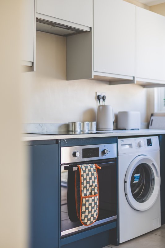 Modern kitchen with white cabinets, integrated oven, washing machine and countertop appliances