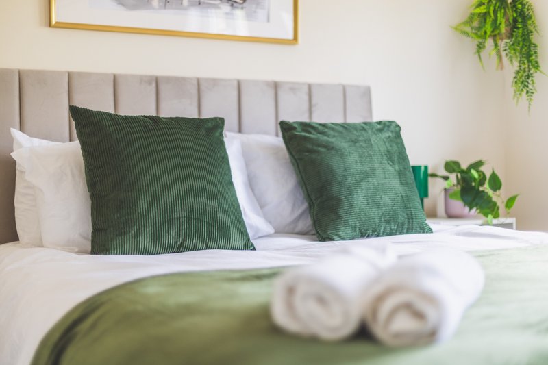 Bedroom with upholstered headboard, green and white pillows, white towels, and potted plants