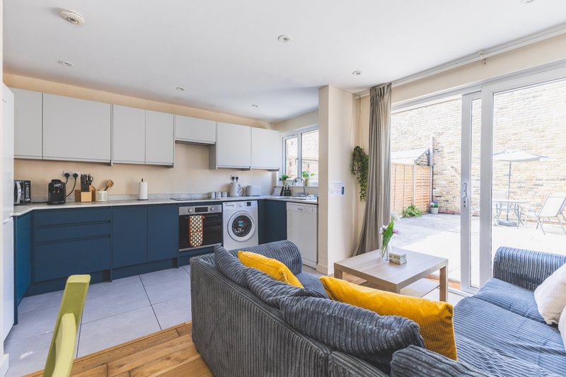 Open-plan kitchen and living area with blue cabinetry, sofa, and garden view
