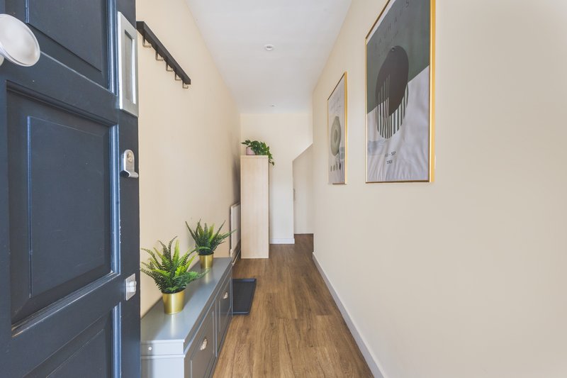 Narrow hallway with dark blue door, wooden floor, potted plants and wall art