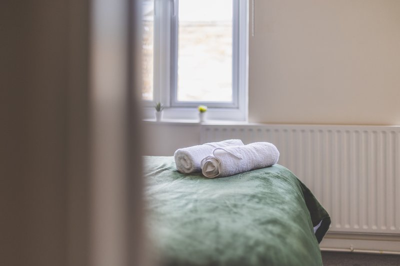 Bedroom with rolled white towels on green bedspread, radiator and window