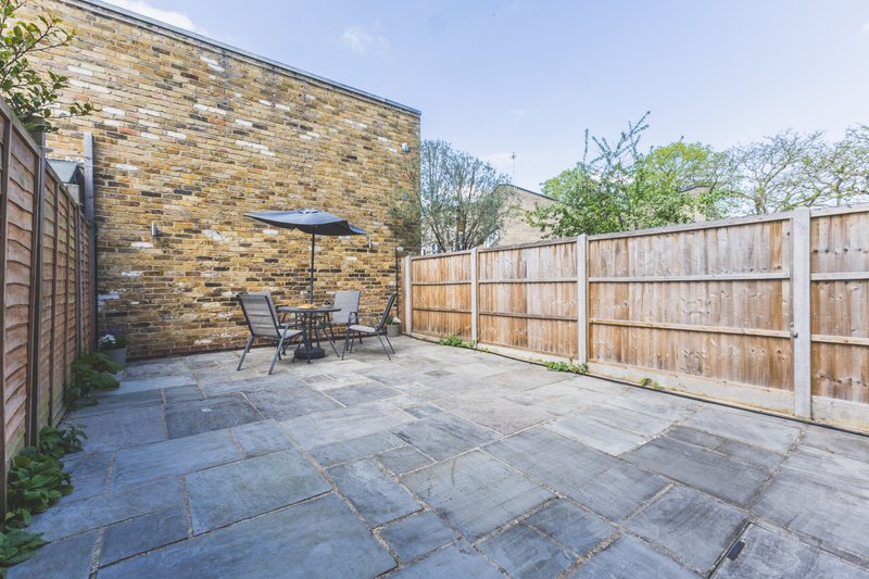 Paved patio area with outdoor seating, brick wall, and wooden fence surrounding garden