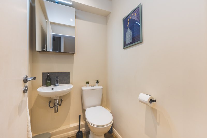 Compact bathroom with toilet, pedestal sink, mirror cabinet and wall art