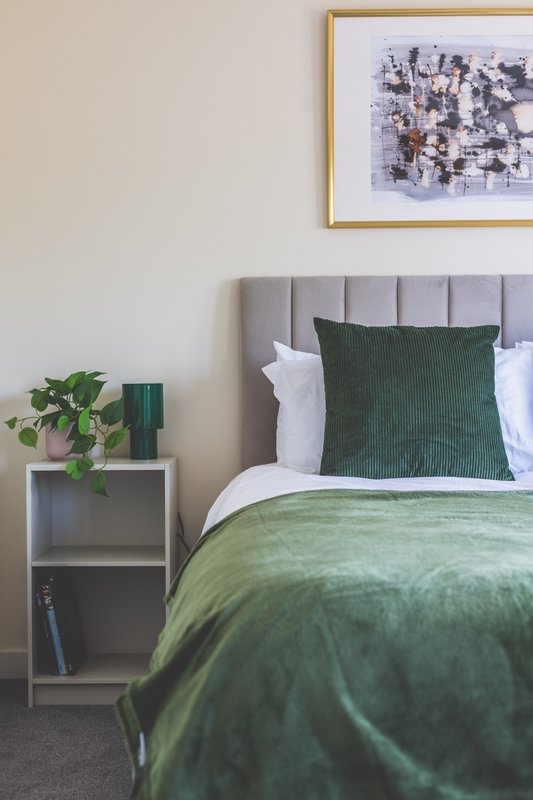 Bedroom with grey upholstered headboard, green bedding, white pillows, and framed wall art