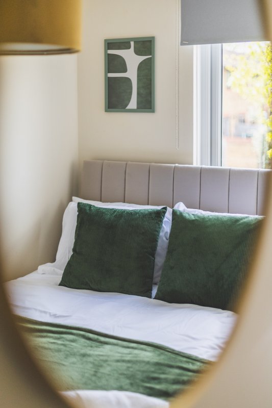 Bedroom with upholstered headboard, green cushions, white bedding and wall art