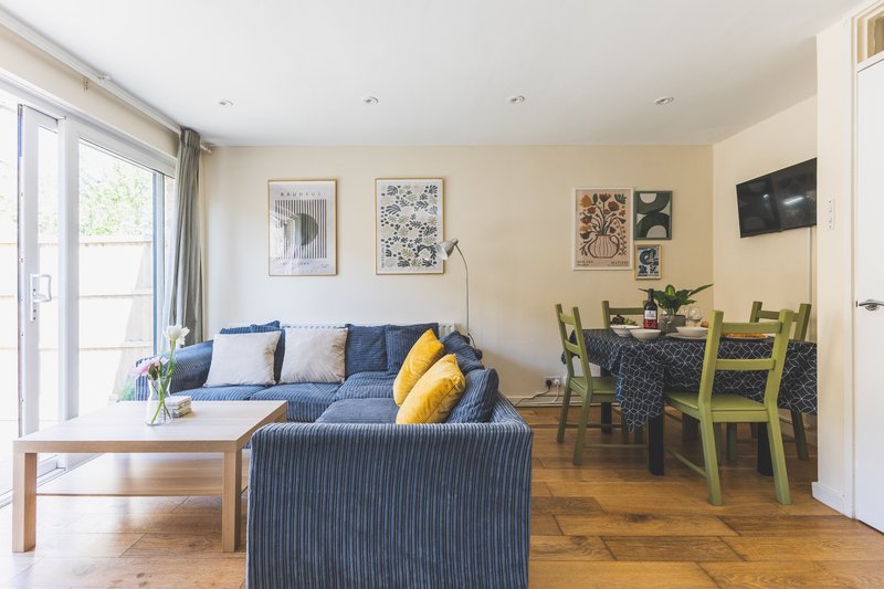 Open-plan living room with blue sofa, wooden coffee table, and dining area with green chairs