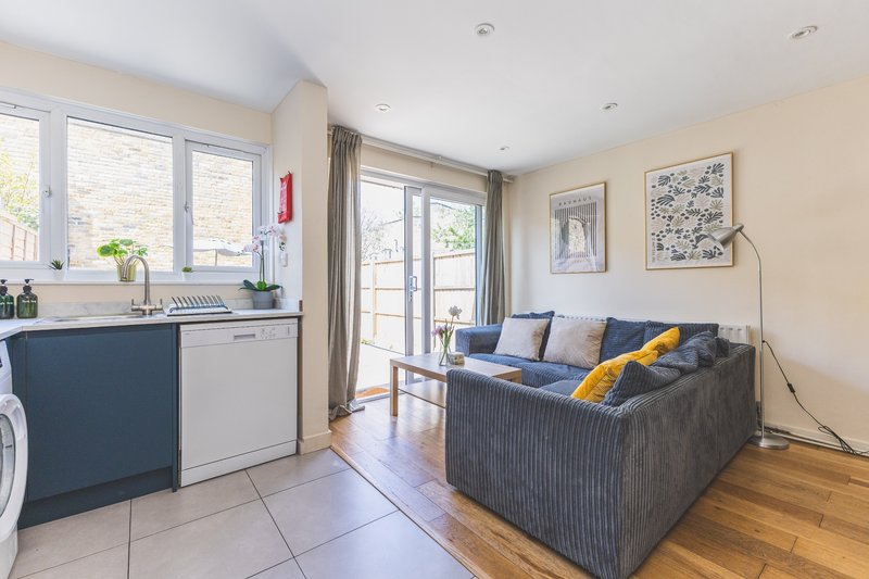 Open-plan living space with kitchenette, gray sofa, wooden flooring and garden access