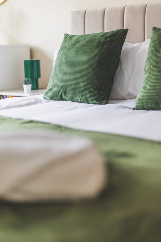 Modern bedroom with upholstered headboard, green and white pillows, and white bedding