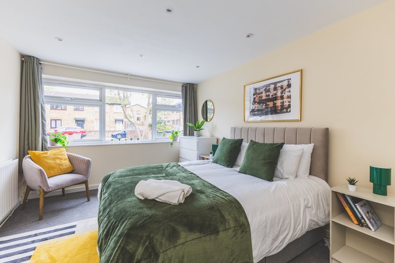 Bright bedroom with double bed, green bedding, armchair, window overlooking street, cream walls