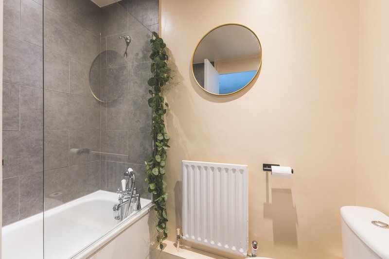 Modern bathroom with bathtub, glass shower screen, radiator and round mirror