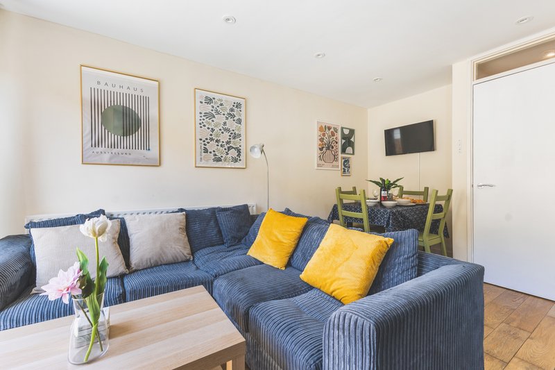 Living room with blue sectional sofa, yellow cushions, framed artwork, and wooden coffee table