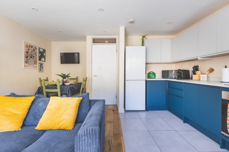 Open-plan living and kitchen with blue sofa, yellow cushions, blue cabinetry, and white appliances