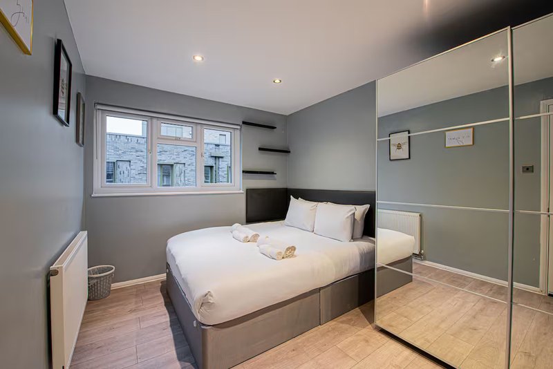 Modern bedroom with double bed, mirrored wardrobe, window and wooden flooring