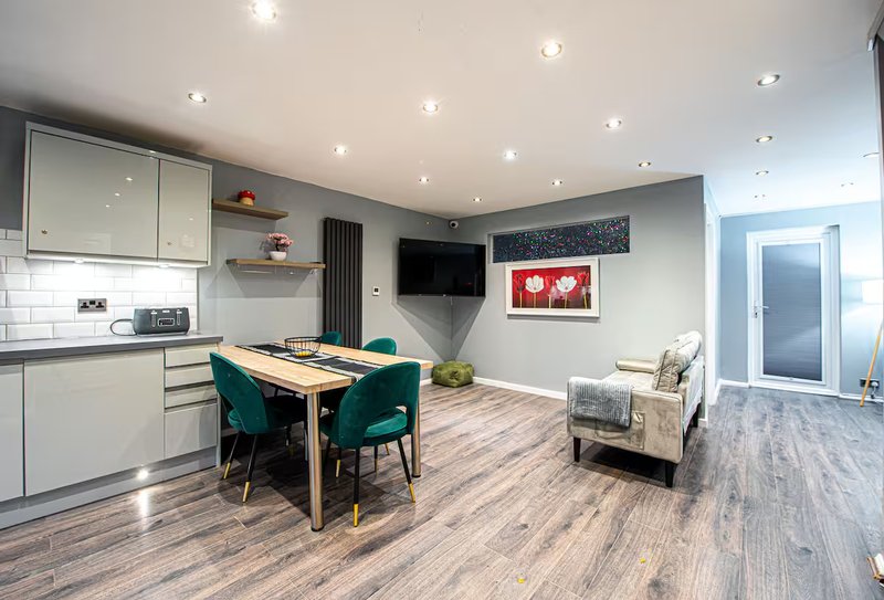 Open-plan kitchen and dining area with dining table, teal chairs, cream cabinetry, wooden flooring