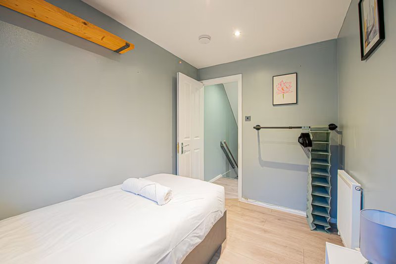 Bedroom with single bed, wooden floor, blue-grey walls and ensuite bathroom door