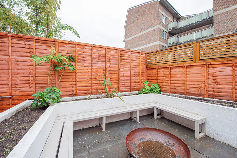 Outdoor patio area with wooden benches, fire pit, planters and red wooden fence