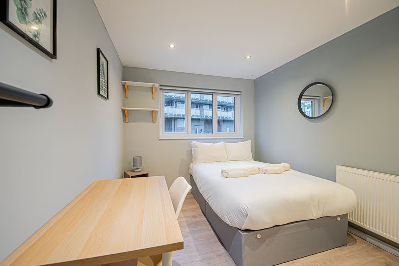 Bright bedroom with single bed, wooden desk, shelving, and large window