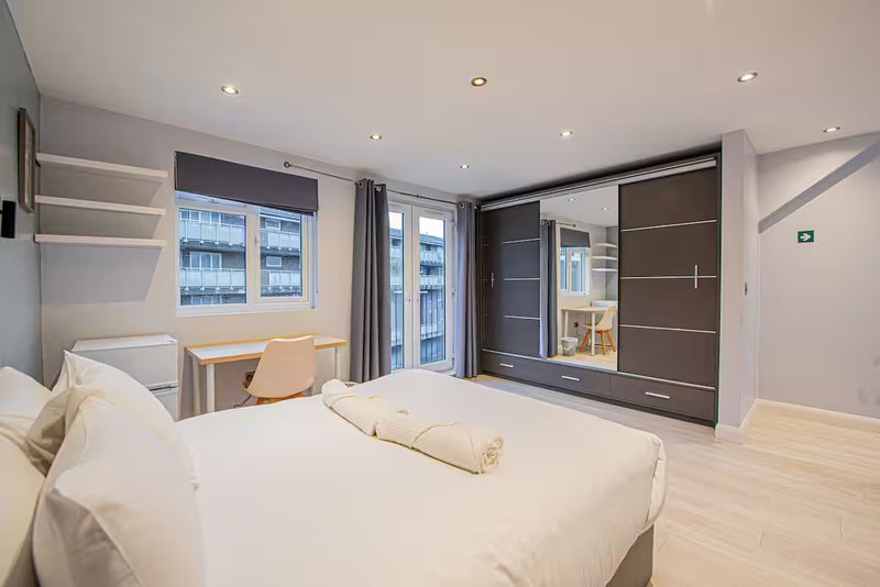 Modern bedroom with double bed, wooden floor, wardrobe and city views