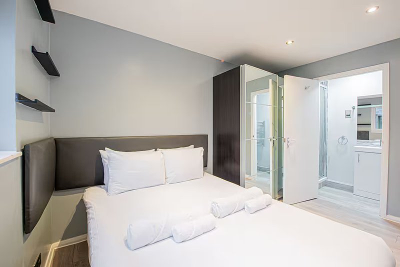 Modern bedroom with double bed, grey headboard, ensuite bathroom visible through open door