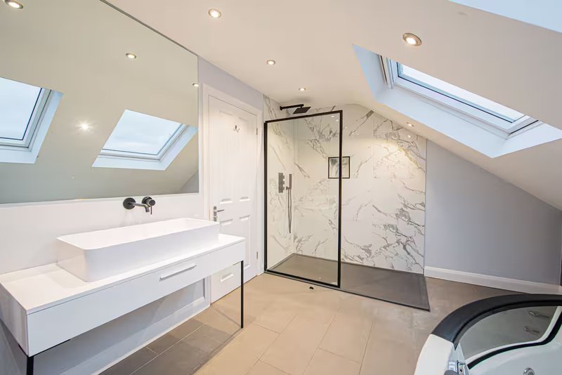 Modern attic bathroom with marble shower enclosure, white vanity, and skylights