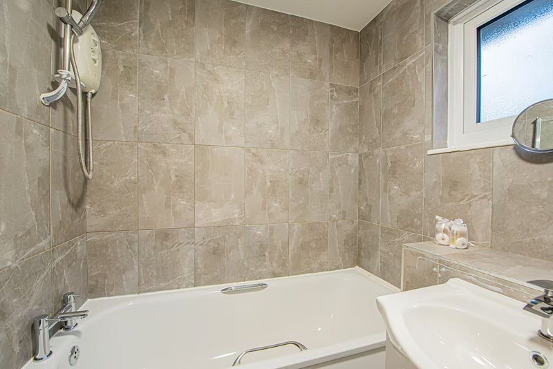 Modern bathroom with bathtub, sink, tiled walls, shower head and window