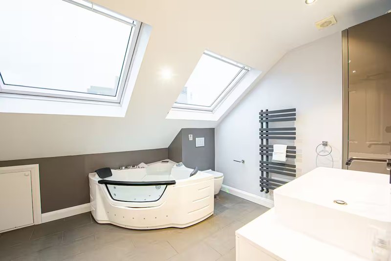 Modern bathroom with corner bathtub, double sinks, heated towel rail and skylights