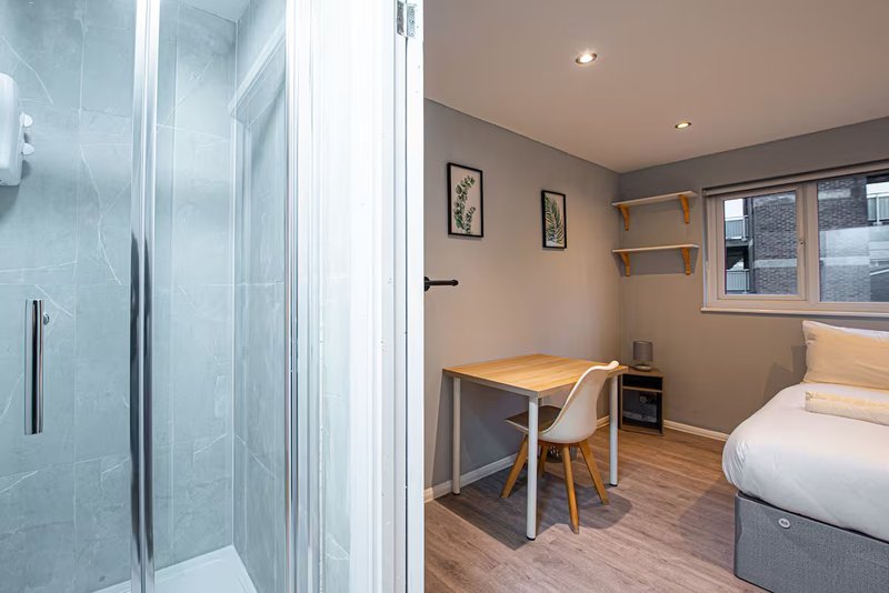 Modern bedroom with ensuite shower, desk, chair, wooden flooring and bed