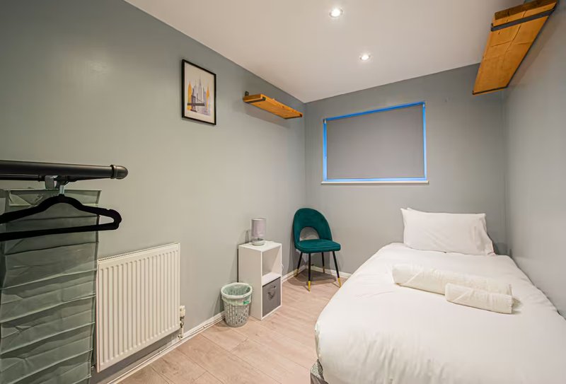 Compact bedroom with single bed, teal chair, radiator, and wooden floor