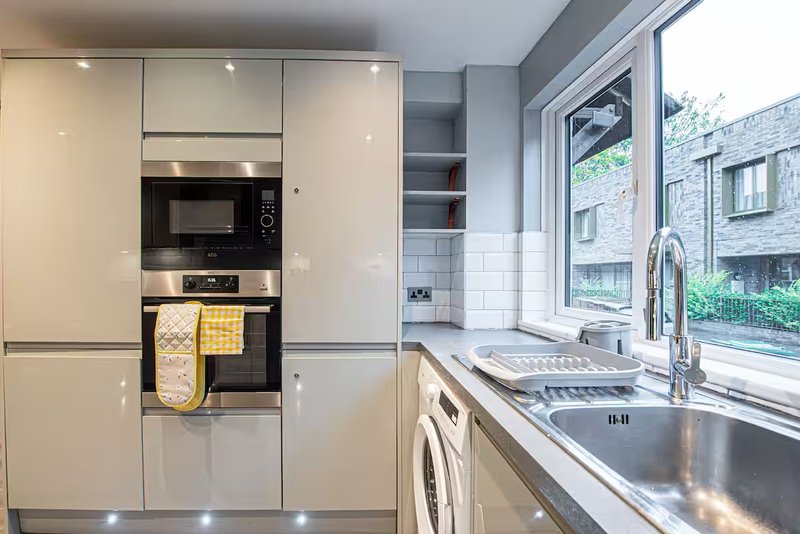 Modern kitchen with cream cabinetry, stainless steel sink, microwave and window overlooking street