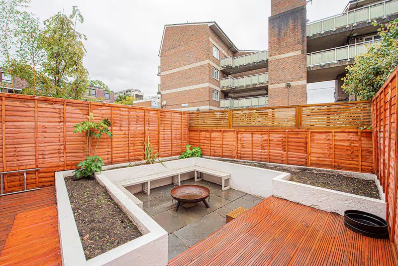 Shared courtyard with wooden decking, raised planter beds, fire pit, and orange fence