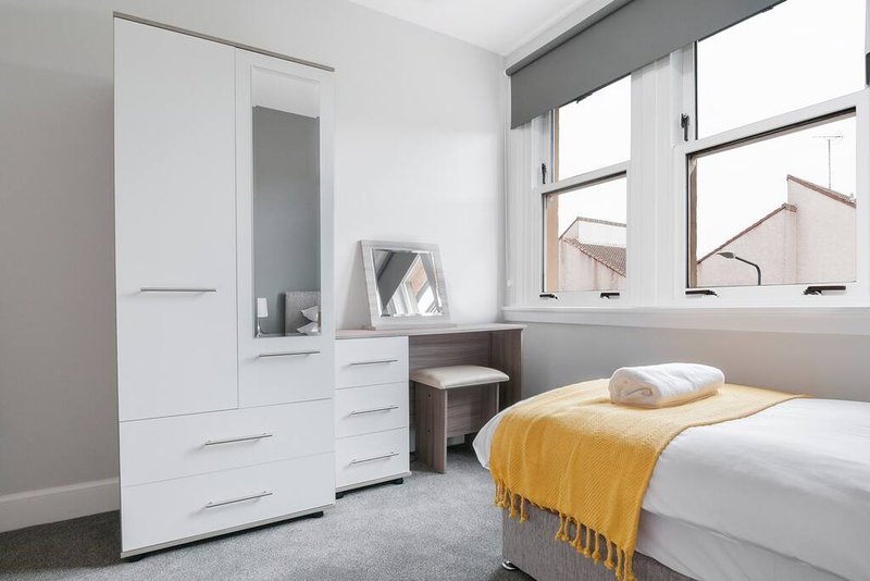 Modern bedroom with single bed, white wardrobe, desk, mirror and large windows