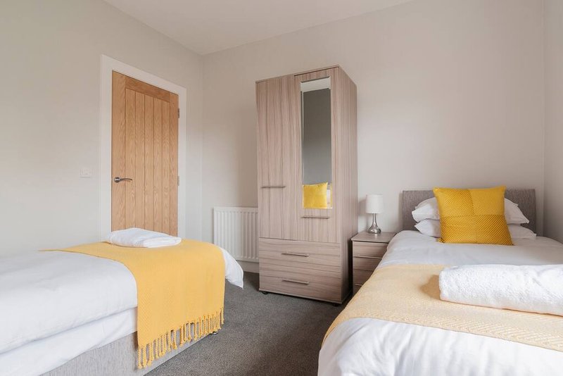 Bright twin bedroom with two single beds, wooden wardrobe and yellow accent cushions