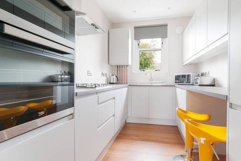 Modern kitchen with white cabinetry, stainless steel appliances, wooden flooring and yellow bar stools
