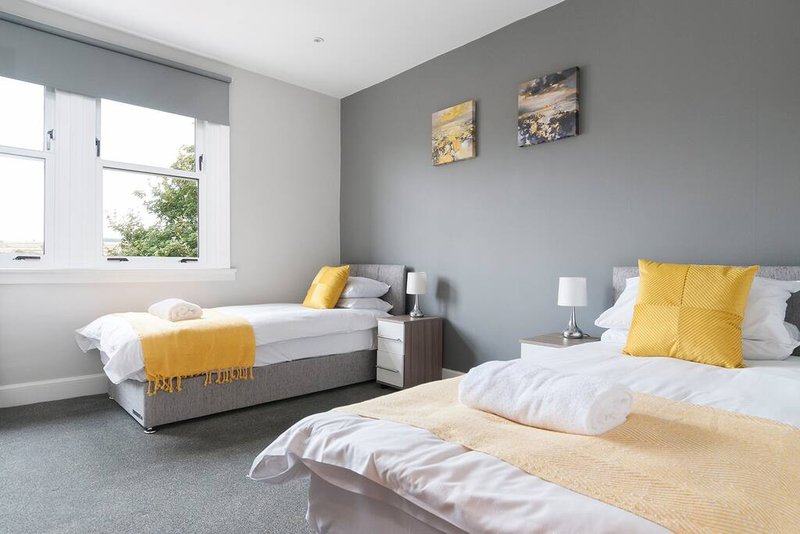 Bright bedroom with two beds, yellow cushions, grey walls, and window with natural light