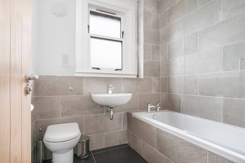 Clean bathroom with toilet, wall-mounted sink, bathtub and tiled walls