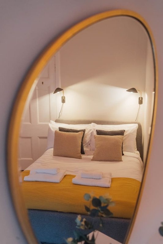 Bedroom reflected in round mirror, showing bed with cushions and white towels