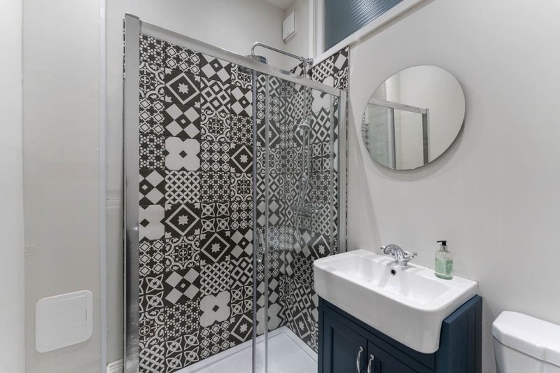 Modern bathroom with patterned shower enclosure, white sink, round mirror and toilet