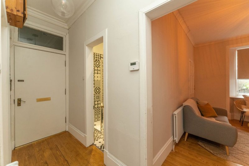 Hallway with wooden flooring, white walls, and doorways leading to orange-painted room with sofa