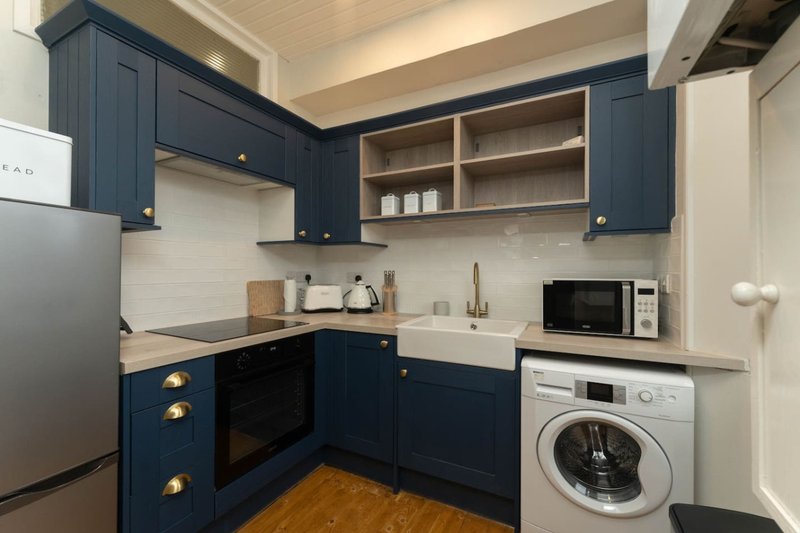 Modern kitchen with dark blue cabinetry, white countertops, stainless steel appliances and integrated washing machine
