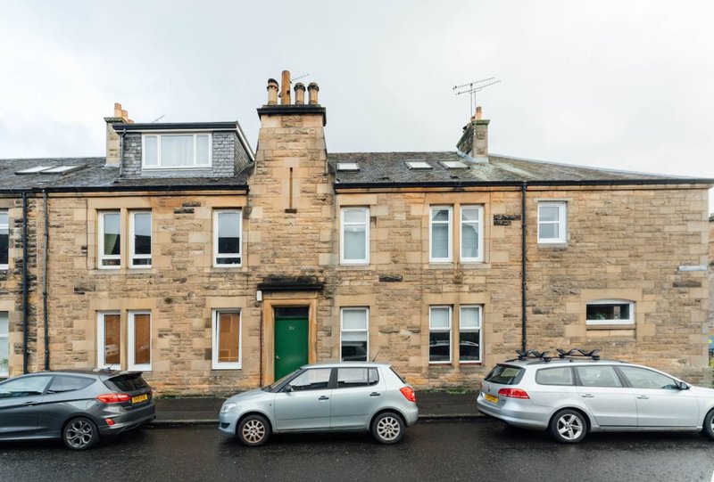 Stone-built terraced house with green door, multiple windows, and parked cars on street